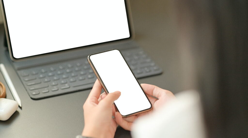 Close up image of the hand of a businesswoman is using a blank screen smartphone with a laptop.