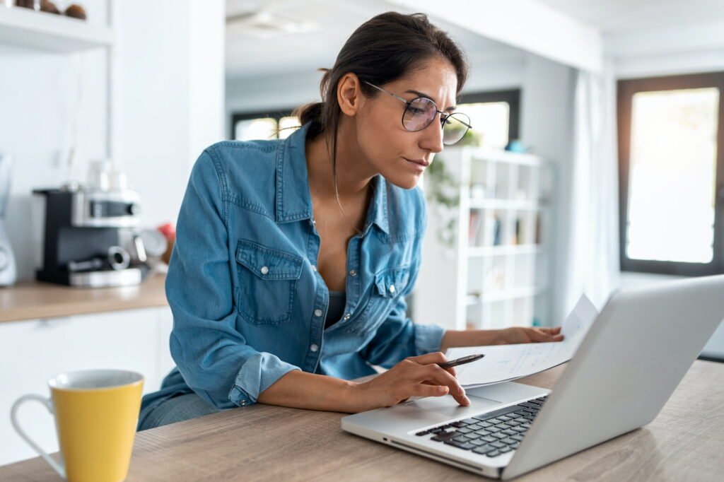 Pretty young woman working with laptop during morning coffee in the kitchen at home.