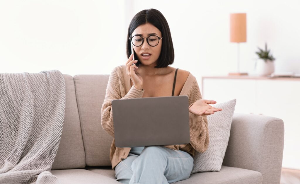 Frustrated asian woman talking on mobile phone sitting on sofa to Comcast