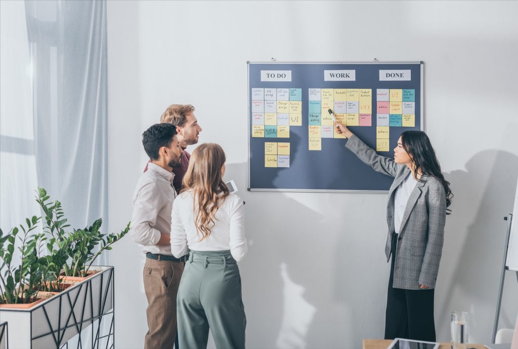 attractive asian scrum master pointing at db design letters on sticky note near businessmen